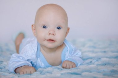 Sevimli mavi gözlü küçük çocuk yatakta uzanıyor ve kameraya şüpheyle bakıyor. Seçili odak, bulanık arkaplan.