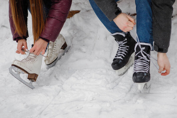 Молодой парень и девушка кружева коньки сидя на скамейке возле катка в зимнем парке.