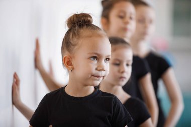 Kız jimnastikçiler peş peşe eğitim sırasında duvara tutunuyorlar. Siyah taytlar, topuz şeklinde saçlar, koreografi, dikkat. Seçili Odaklanma