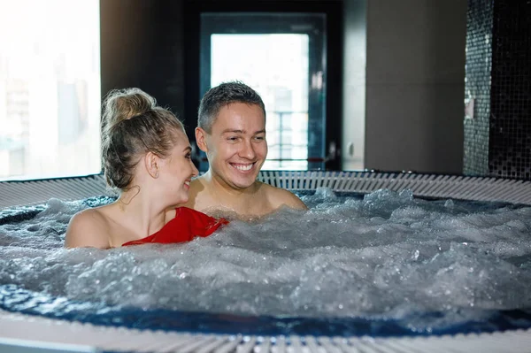 年轻貌美的夫妇正在按摩浴缸里放松 蓝色泡沫般的水 快乐的微笑 融合在一起 有选择的重点 模糊的背景 — 图库照片