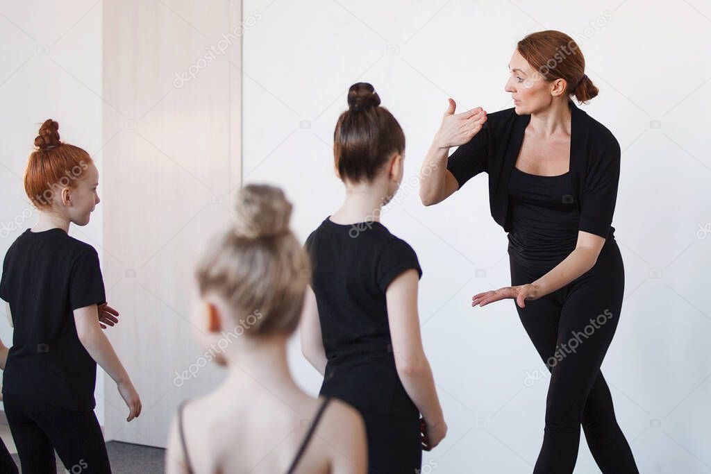 Female trainer shows dance poses in ballet classes. Selected Focus. Black leotard, hair in a bun, white socks.
