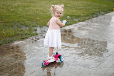Şehir caddesinde bir su birikintisinin ortasında at kuyruklu küçük sarışın kız..
