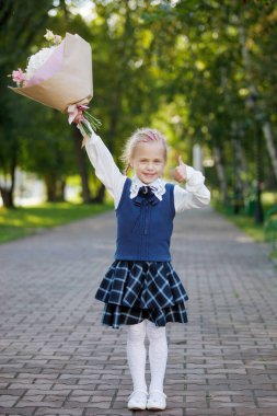 Okul yılının başında elinde bir buket çiçekle bir şehir parkında üniformalı bir kız öğrenci. İlk kez birinci sınıfta..