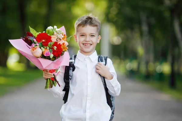 School teenager with a bouquet of flowers at the start of the school year in a white shirt in a city park. The first time in first class.