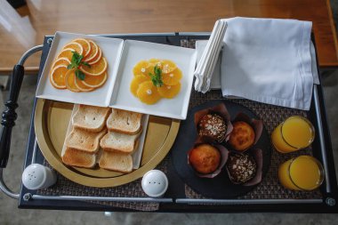 Kahvaltı tepsisi otel odasında. Tost, portakal tabağı, meyve suyu bardakları, peçeteler. Düz yatıyordu.