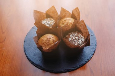 Tahta kahverengi bir masada, siyah tabakta badem olan dört muffin. Seçili odak.