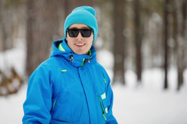 Güneş gözlüklü genç, yakışıklı adam kışın dışarıda gülümsüyor.