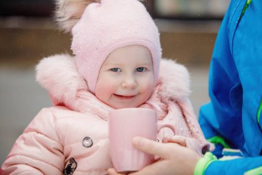 Pembe tulumlu bir kız çocuğu ve bir kupa sıcak çay. Şehir parkında güneşli bir kış günü, açık havada..