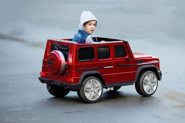 Chłopiec Kurtce Kapturem Jeździ Czerwonym Samochodziku Dla Dzieci — Zdjęcie stockowe