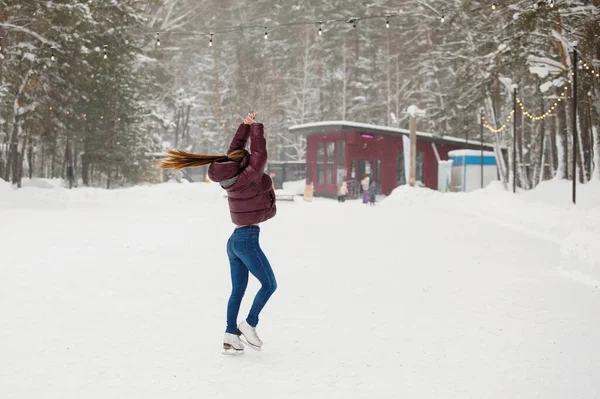 若い女の子は屋外の冬の公園のアイスリンクでスケートをしています 暖かい服 ニット帽 雪のドリフト ぼやけた背景 — ストック写真