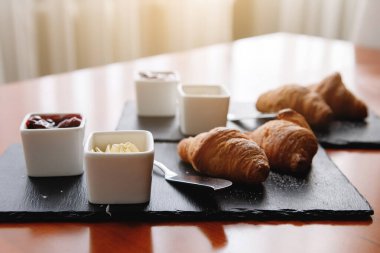 Kahvaltınızı siyah tabakta servis ediyorsunuz. Kruvasan, reçel ve çatal bıçak. Seçici odak.