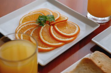 Masadaki beyaz tabakta kahvaltı servisi. Tost, çay tabağında portakal, otel odasında bir bardak meyve suyu..