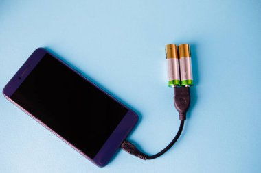 İki AA alkalin pil akıllı telefonu şarj eder. Beslenmek. Mavi arka plan. Temiz enerjinin sembolü. Çevre dostu.