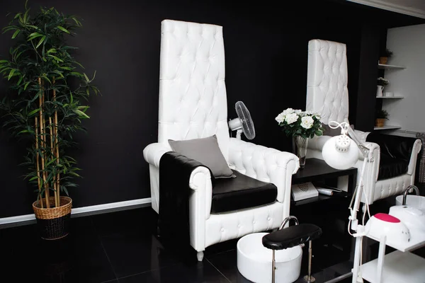 Beauty Salon Interior. Black and white gamma. The workplace of the pedicure master with huge chairs, footrests.