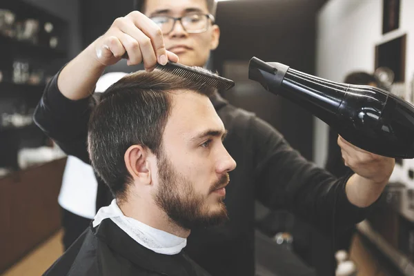 Man hairdresser uses hairdryer to style hair beautifully for client,  barbershop - Stock Image - Everypixel