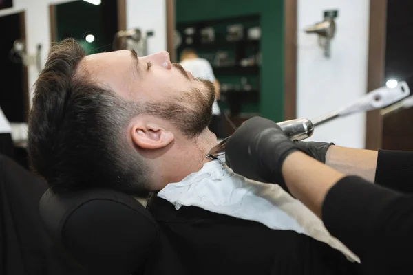 在理发店为有魅力的年轻人做理发师的特写工作 刮胡子 用直角剃须刀刮掉 — 图库照片