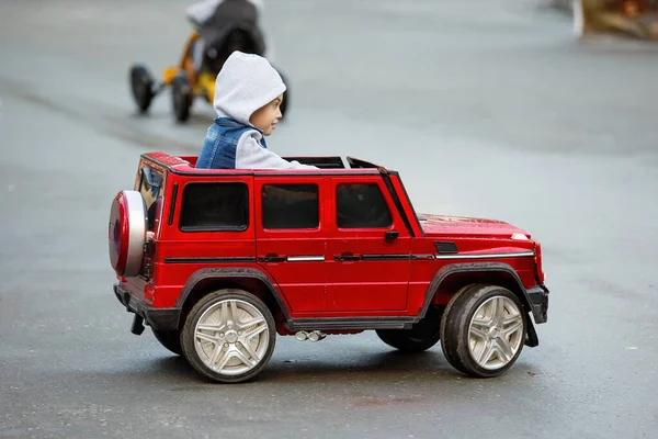 Chłopiec Kurtce Kapturem Jeździ Czerwonym Samochodziku Dla Dzieci — Zdjęcie stockowe