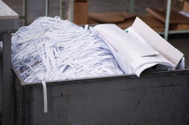 İnce dilimlenmiş beyaz kağıt şeritleri ve kağıt yığınları baskı makinesindeki bir çöp konteynırında..