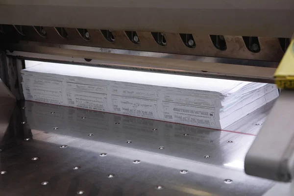 Cutting piles of paper with a guillotine blade in a printing house.