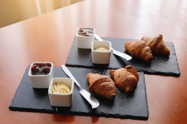 Kahvaltınızı siyah tabakta servis ediyorsunuz. Kruvasan, reçel ve çatal bıçak. Seçici odak.