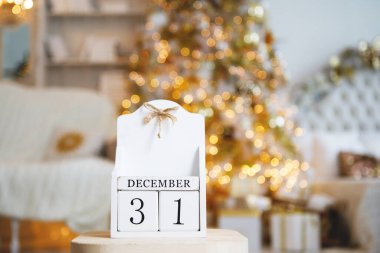 Üzerinde 31 Aralık tarihli ahşap küplerin olduğu eski bir takvim yanan bulanık ışıklarla bir Noel ağacının arka planında. Önplanda seçili odak.
