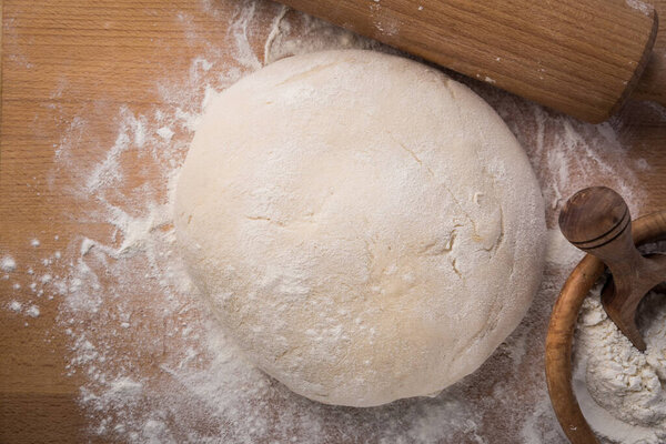 Homemade yeast dough freshly prepared for pizza or bread on wooden background.. Home cooking concept.