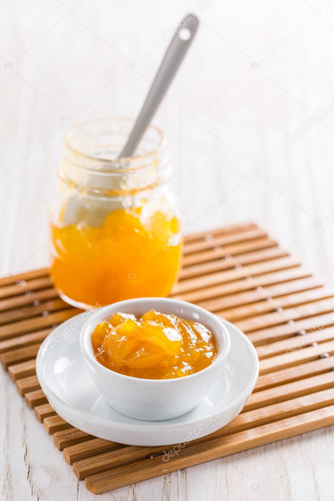 Lemon curd or fruit jelly in small bowl and glass jar for breakfast or baking on wooden background.