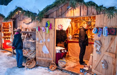 Ahşap kulübelerde aydınlatılmış dükkanlar, hediyeler ve el yapımı dekorasyonlarla romantik Noel pazarı..