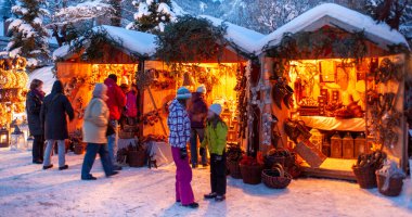 Ahşap kulübelerde aydınlatılmış dükkanlar, hediyeler ve el yapımı dekorasyonlarla romantik Noel pazarı..