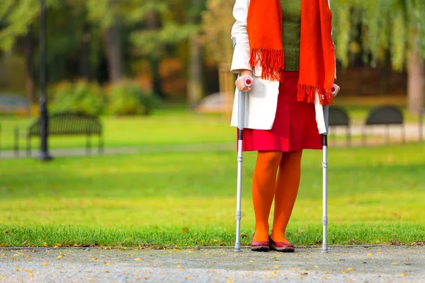 woman in colorful clothes standing on crutches in the autumnal park