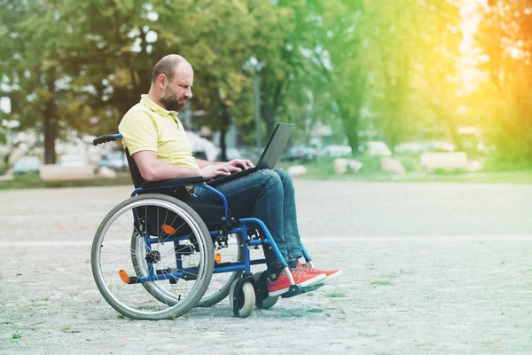 Uomo sulla sedia a rotelle che lavora sul computer portatile — Foto Stock