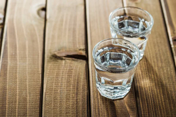 Vodka in shot glass. Transparent alcohol on wooden table.