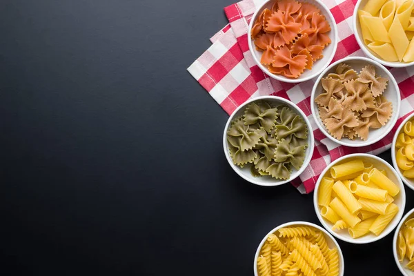 Various types of italian pasta in bowl on black background.