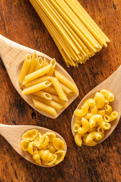 在木制桌子上的木制勺子中的各种意大利生面食 顶部视图 — 图库照片