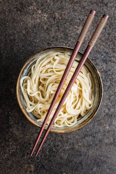 Cooked udon noodles. Traditional Japanese noodles in bowl on black table.