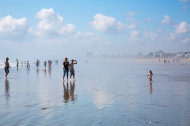 Old Orchard Beach, Maine, USA - September 1, 2014: People enjoying sea and sunshine. Heat haze of evaporating water, reflected blue sky. clipart