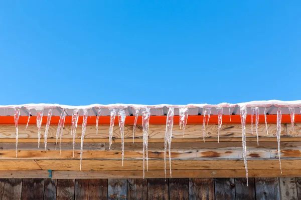 在加拿大的一个冬天 冰柱挂在屋顶上 蓝色的天空与橙色油漆的木结构建筑 最小风格的蓝色 有文字空间 — 图库照片