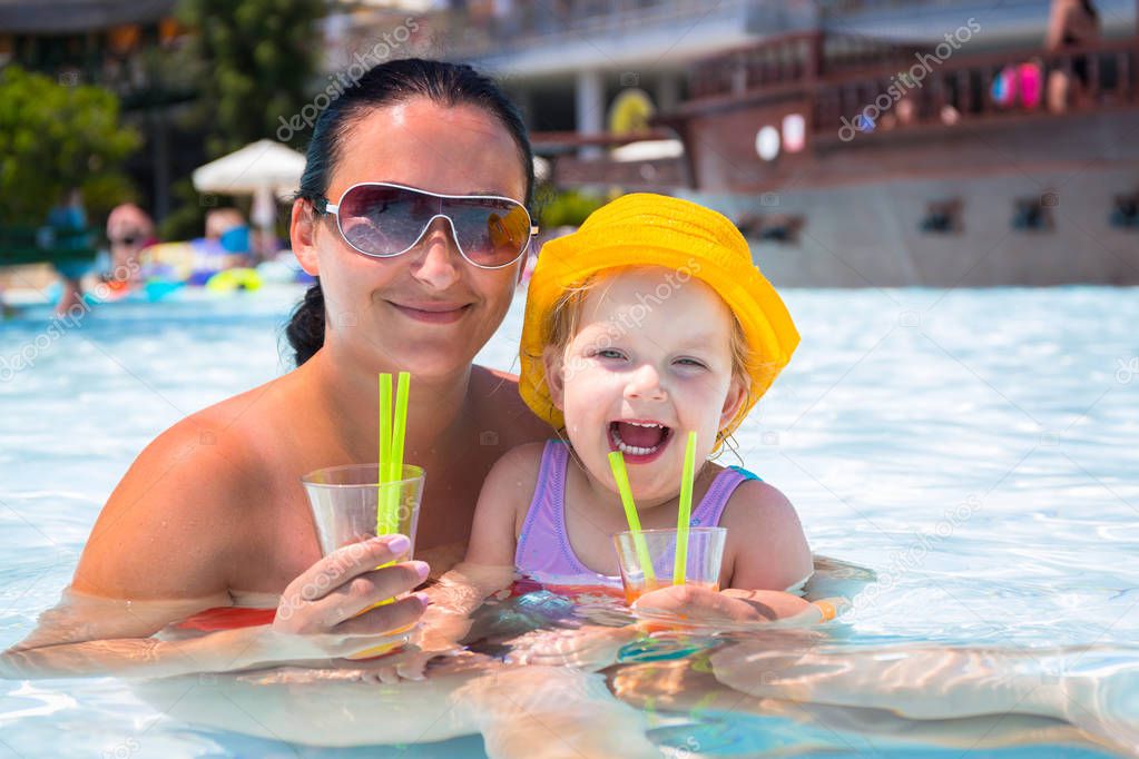 Mom with little daughter drinking juice at the pool on summer holidays