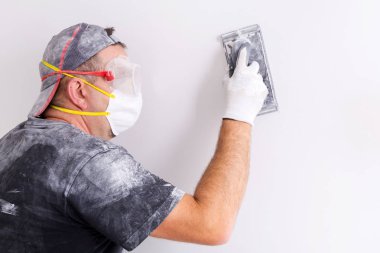 Sıvacı toz maskesi ve duvar parlatma, googles giyiyor. Ev yenileme kavramı.