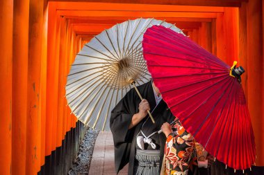 Couple with traditional japanese umbrellas posing at torii gates in Kyoto clipart