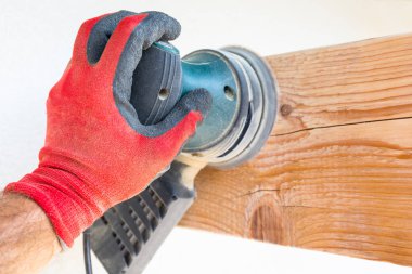 Marangoz, kirişi ahşap bir elektrikli öğütücüyle elle parlatır.