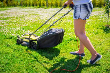 Woman cutting grass in her yard with lawn mower. clipart