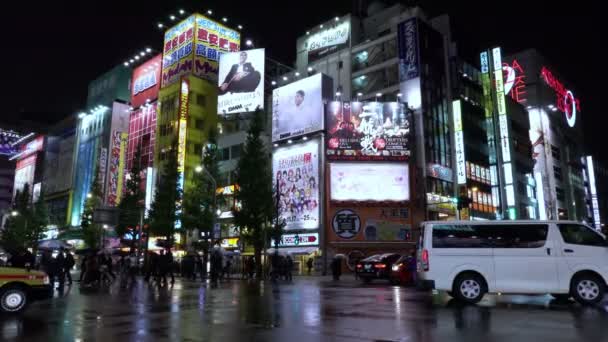 Неоновые огни и рекламные щиты на зданиях в Акихабаре в дождливую ночь, Токио, Япония — стоковое видео