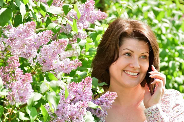 Happy woman with phone near blooming lilac — Stock Photo, Image