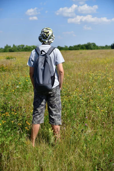 teenager with backpack is standing with his back on a meadow