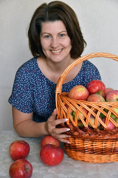 Femme avec un panier de pommes rouges s'assoit à table — Photo