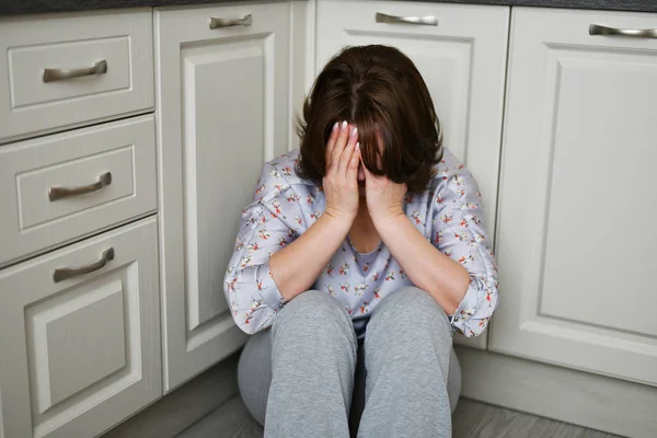 Mujer está sentada en el suelo de la cocina cubriéndose la cara con las manos. Depresión, dolor o frustración — Foto de Stock