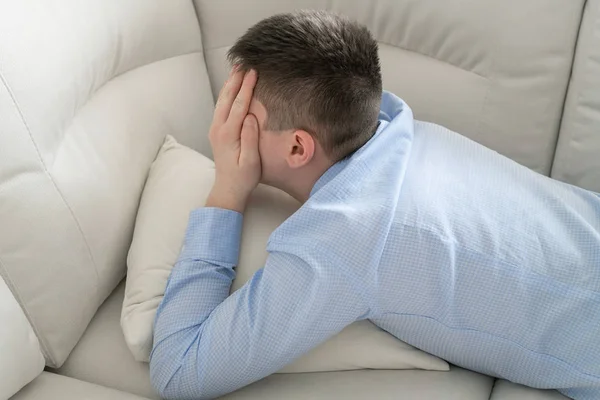 Depresif genç elleri ile yüzünü kaplayan kanepede yatan — Stok fotoğraf