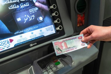 Abu Dabi, Bae - 29 Mart. 2019. Abu Dabi Ticaret Bankası arka plan Atm karşı elinde 100 dirhem