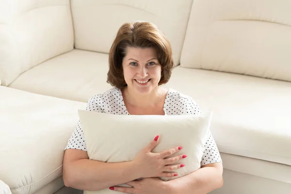 Mujer sonriente sentada con almohada junto al sofá — Foto de Stock